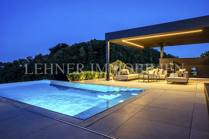 Beleuchtete Poolterrasse mit Lounge und Pergola in der Dämmerung